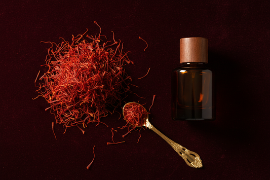 Vivid crimson saffron threads on burgundy velvet with gold spoon and perfume oil bottle in warm jewel-toned light