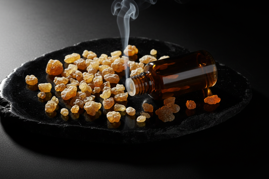 Translucent golden frankincense tears and resin chunks with wisp of incense smoke and perfume oil bottle on dark obsidian